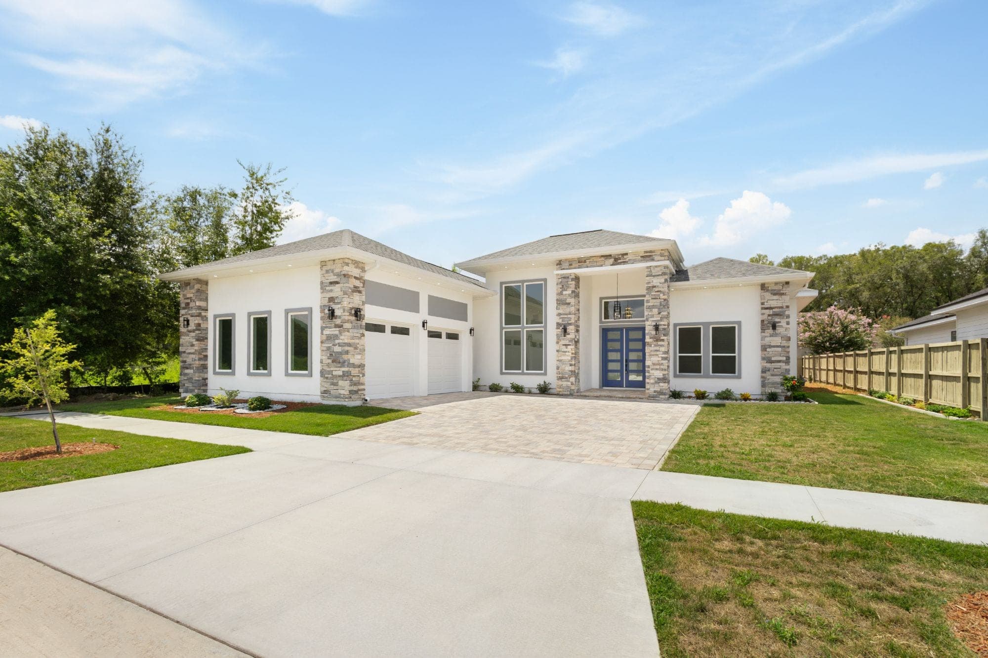 Contemporary stucco home with stone columns and a blue double door
